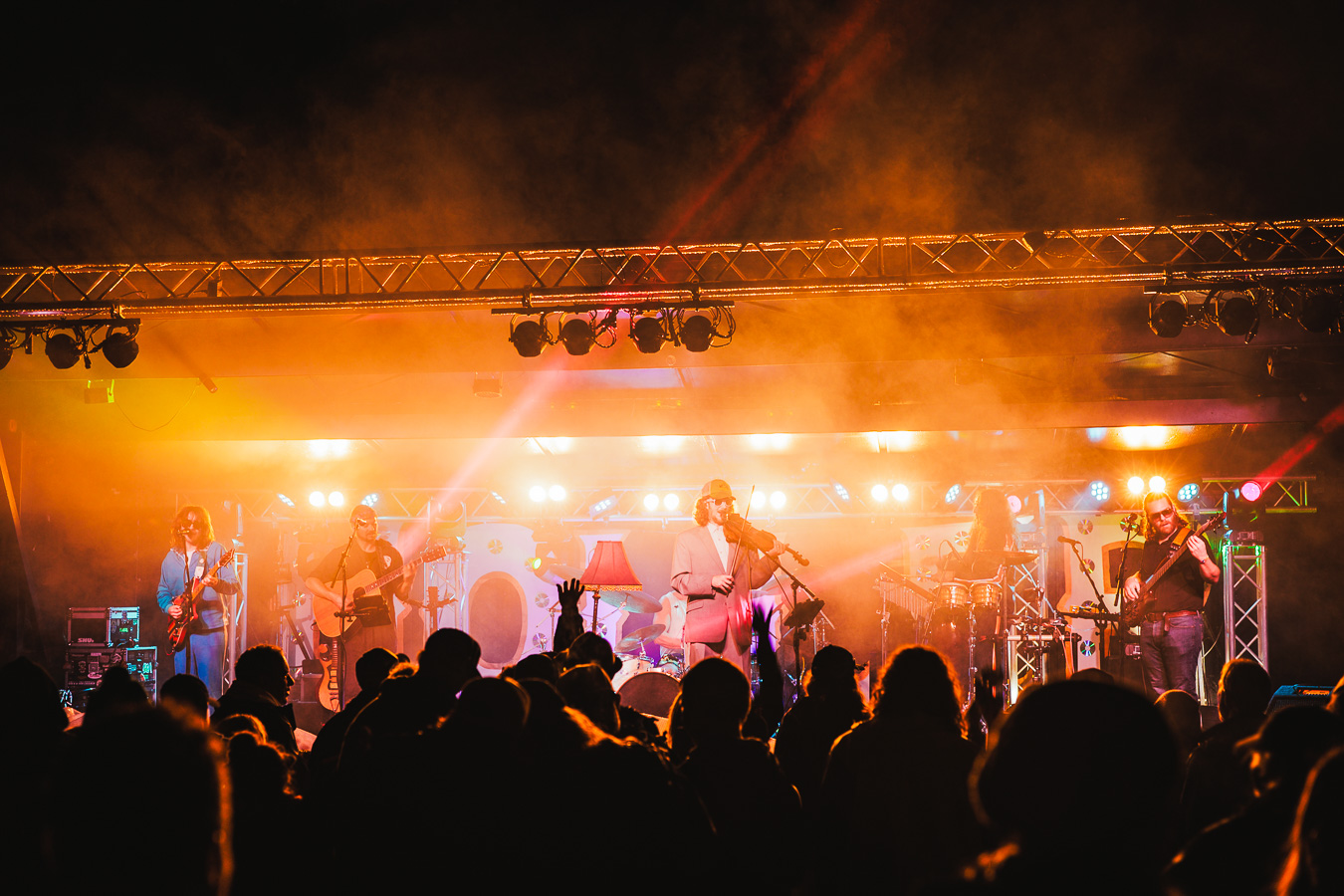 A crowd in silhouette in front of a stage lit orange at night at Jennings Holler
