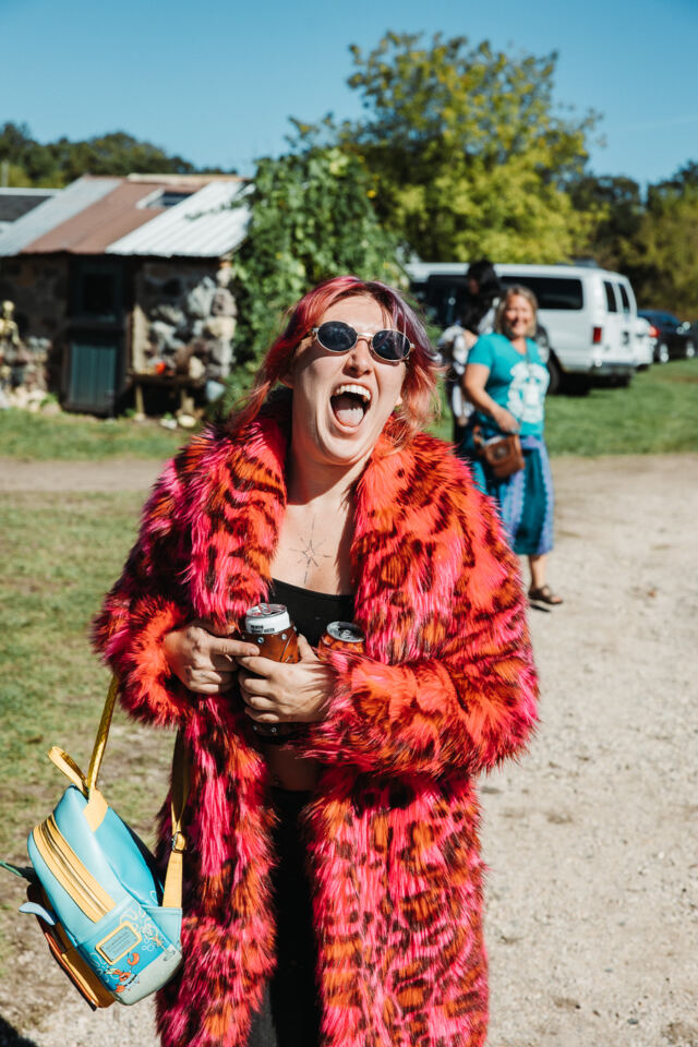 A festival-goer in a pink fur coat laughing on the grounds